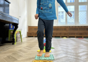 Dziecko chodzi gołymi stopami po ścieżce sensorycznej.