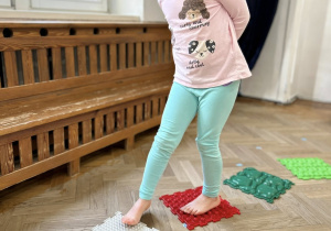 Dziecko chodzi gołymi stopami po ścieżce sensorycznej.