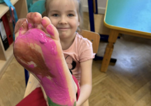 Dziewczynka pokazuje pomalowaną farbą stopę.