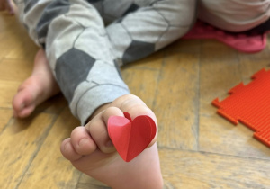 Dziecko trzyma palcami u stopy serduszko z papieru.