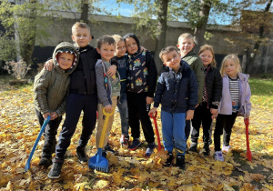 Zdjęcie grupowe - grupa IV. Dzieci stoją w liściach, trzymają grabki.