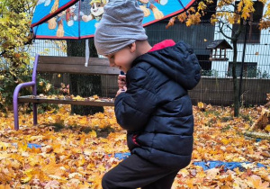 Chłopiec skacze w kałuży, trzyma parasolkę.