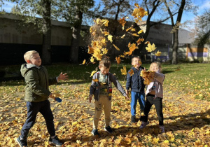 Dzieci podrzucają liście do góry.