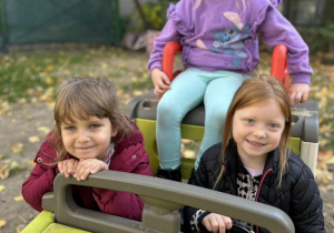 Dziewczynki siedzą w zabawkowym aucie.