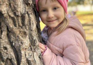 Dziewczynka przytula się do drzewa.