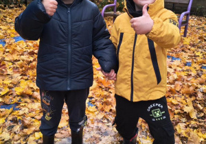 Chłopcy stoją w kałuży i pokazują kciuki.