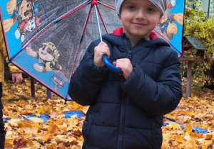 Chłopiec stoi w kałuży i trzyma parasolkę.