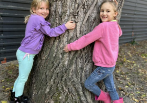 Dziewczynki przytulają się do drzewa.