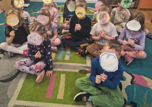 Dzieci trzymają kukiełki emocji. Zasłaniają sobie twarze.