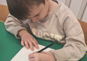 Chłopiec rysuje buzie z wybraną emocją.