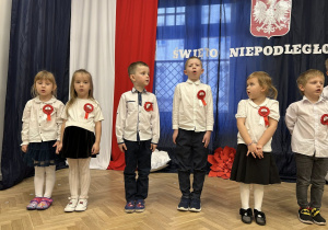 Dzieci stoją w rzędzie na tle dekoracji.