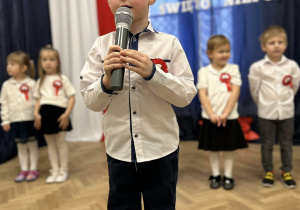 Dziecko stoi na środku sali i mówi wiersz do mikrofonu.