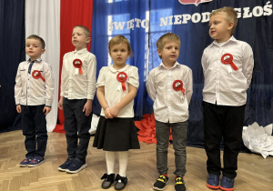 Dzieci stoją w rzędzie na tle dekoracji.