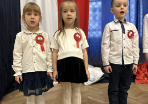 Dzieci stoją w rzędzie na tle dekoracji.