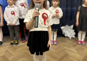 Dziecko stoi na środku sali i mówi wiersz do mikrofonu.