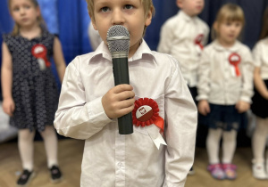 Dziecko stoi na środku sali i mówi wiersz do mikrofonu.
