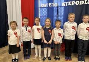 Dzieci stoją w rzędzie na tle dekoracji.