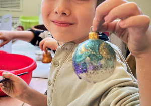 Dziecko pokazuję ozdobioną przez siebie bombkę.