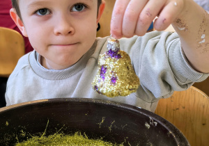 Dziecko pokazuję ozdobioną przez siebie bombkę.