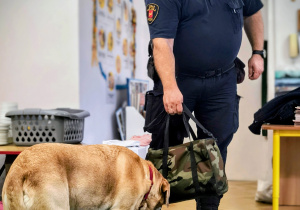 Pan ze straży miejskiej pokazuje dzieciom zadanie, które wykonuje z psem.