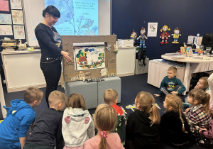 Dzieci siedzą w półkolu i oglądają obrazki związane z wysłuchaną bajką.