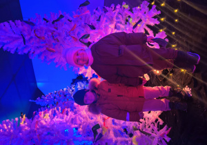 Dzieci stoją na tle dekoracji świątecznej.