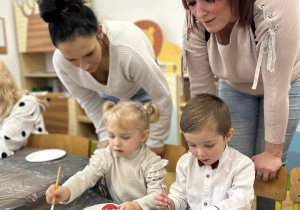 Dzieci z rodzicami ozdabiają styropianowe ozdoby.