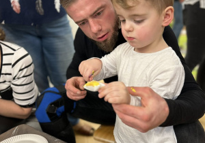 Dzieci z rodzicami ozdabiają styropianowe ozdoby.