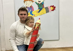 Dziewczynka z tatą trzyma kredkę podczas pasowania.