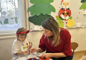 Dziewczynka z mamą przygotowuje świąteczną ozdobę - bombkę.