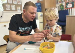 Chłopiec z tatą przygotowuje świąteczną ozdobę - bombkę.