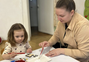 Dziewczynka z mamą przygotowuje świąteczną ozdobę - bombkę.