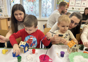 Dzieci wraz z rodzicami ozdabiają domki świąteczne.