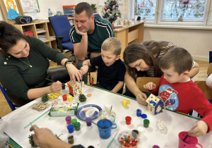Dzieci wraz z rodzicami ozdabiają domki świąteczne.