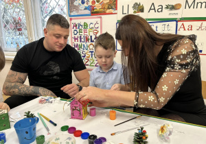 Rodzice z chłopcem ozdabiają domek świąteczny.