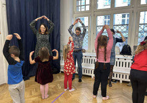 Dzieci wraz z rodzicami trzymają ręce w górze, nad głowami.