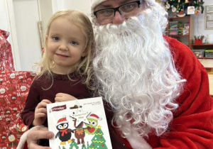 Dziecko siedzi na kolanie Mikołaja i odbiera prezent.