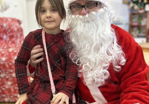 Dziecko siedzi na kolanie Mikołaja i odbiera prezent.