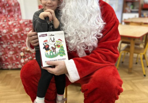 Dziecko siedzi na kolanie Mikołaja i odbiera prezent.