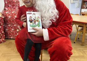 Dziecko siedzi na kolanie Mikołaja i odbiera prezent.