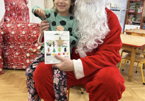 Dziecko siedzi na kolanie Mikołaja i odbiera prezent.