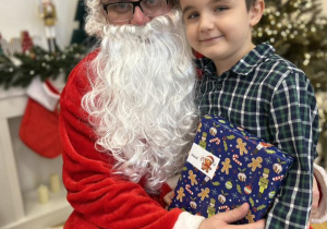 Dziecko siedzi na kolanie Mikołaja i odbiera prezent.