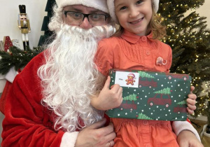 Dziecko siedzi na kolanie Mikołaja i odbiera prezent.
