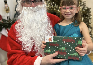 Dziecko siedzi na kolanie Mikołaja i odbiera prezent.