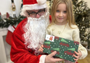 Dziecko siedzi na kolanie Mikołaja i odbiera prezent.