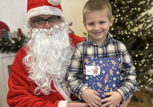 Dziecko siedzi na kolanie Mikołaja i odbiera prezent.