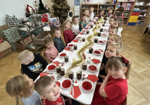 Dzieci siedzą przy stole i jedzą wigilijny obiad.