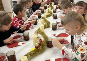 Dzieci siedzą przy stole i jedzą wigilijny obiad.