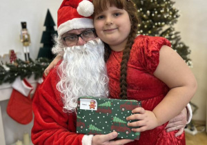 Dziecko siedzi na kolanie Mikołaja i odbiera prezent.