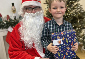 Dziecko siedzi na kolanie Mikołaja i odbiera prezent.